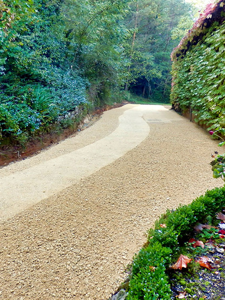 A smooth, freshly installed gravel driveway curving through a lush green area, showcasing a professional installation by ProPave Driveways in Andover.